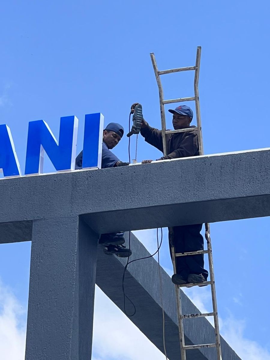 Installer on a ladder fitting large blue letters to a steel gantry
