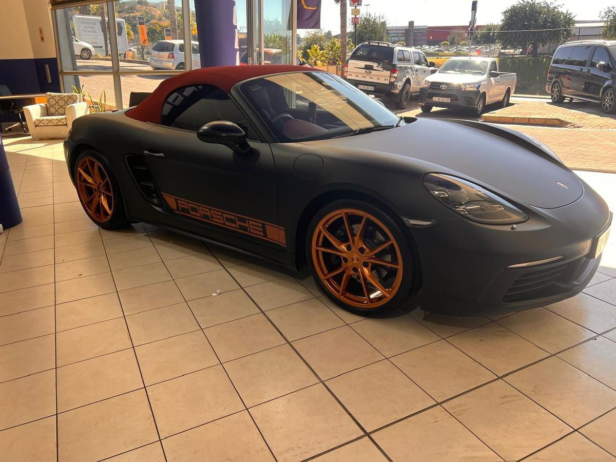 Satin black wrapped Porsche with orange wheel accents in a showroom