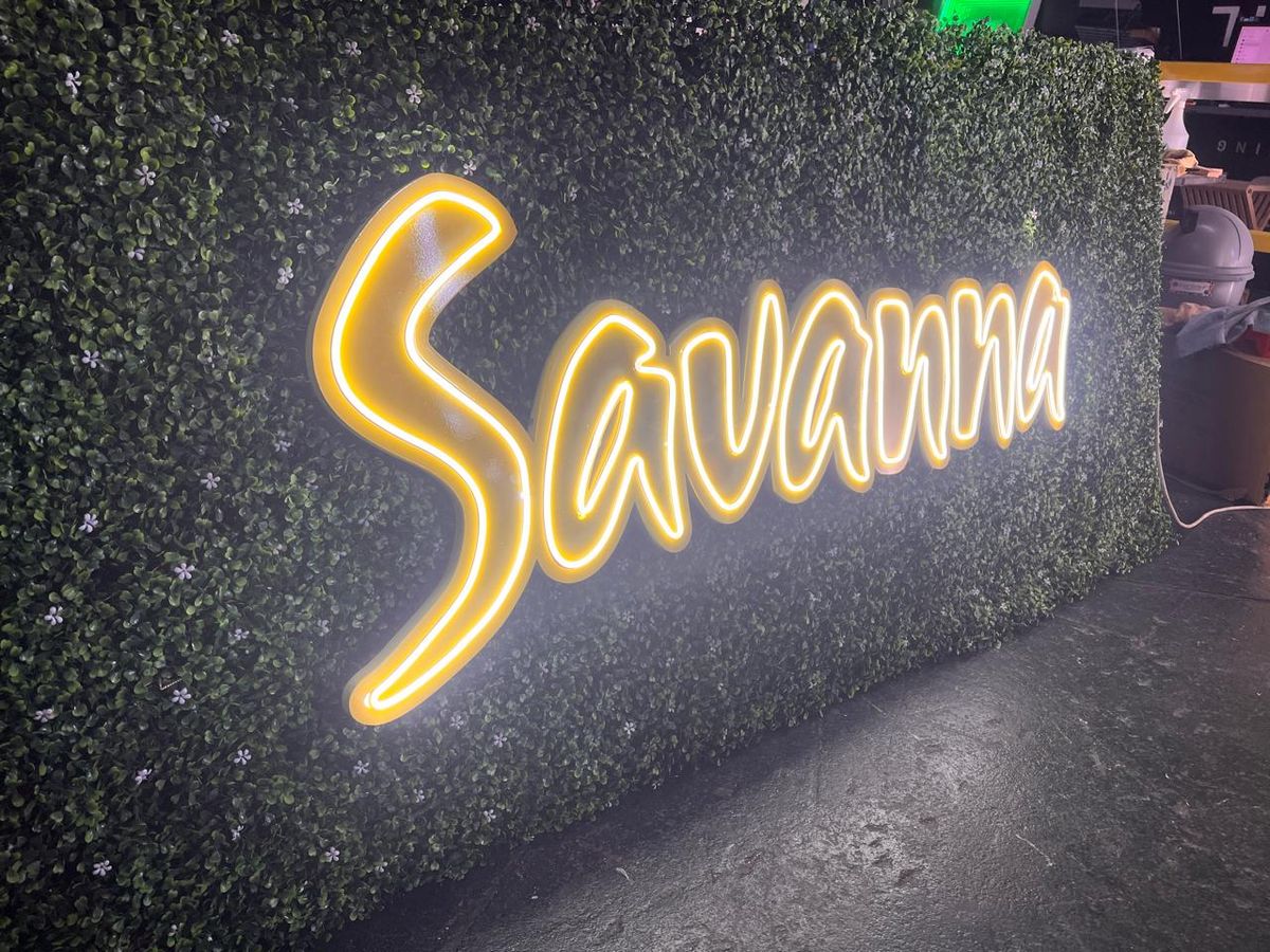 Savanna glowing yellow script sign on a green wall at night