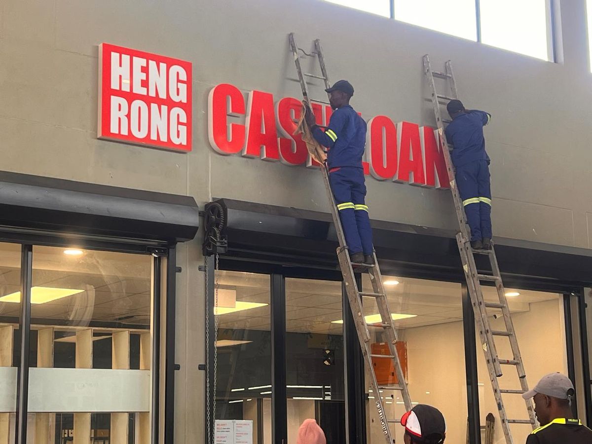Installers on ladders fitting red fascia lettering to a shopfront